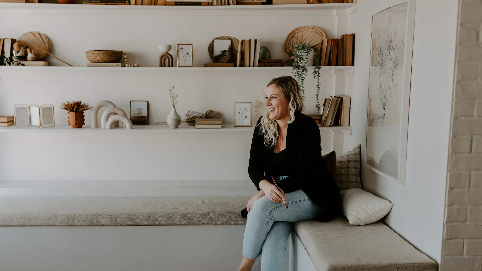Woman sitting on a built-in bench in a cozy room with shelves and decor.