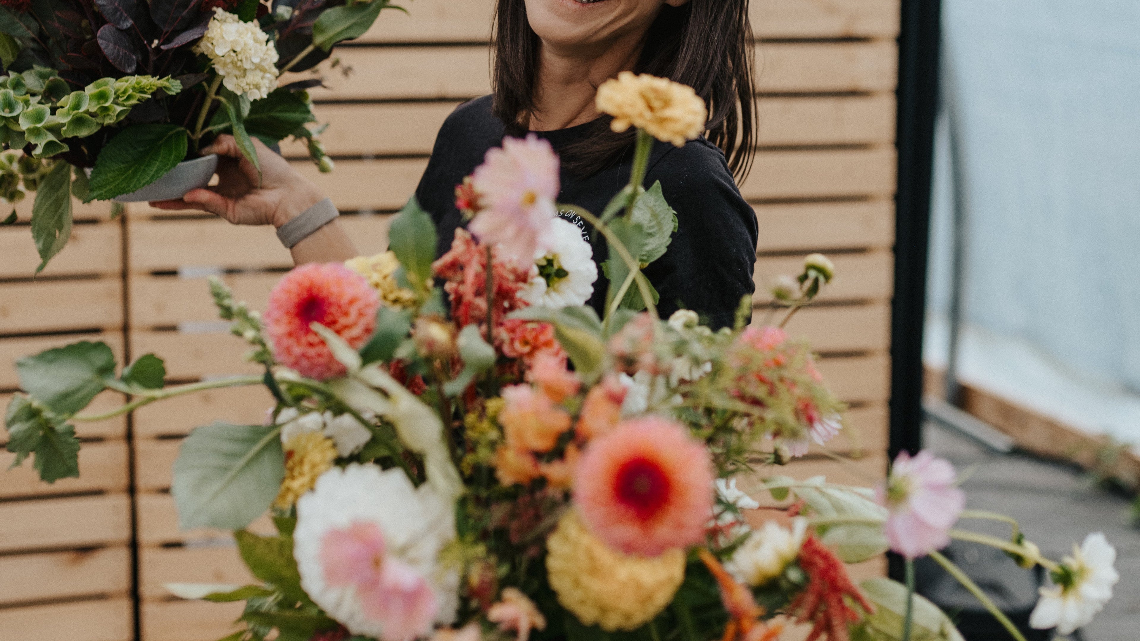 Woman holding a large bouquet of flowers in front of a wooden panel.