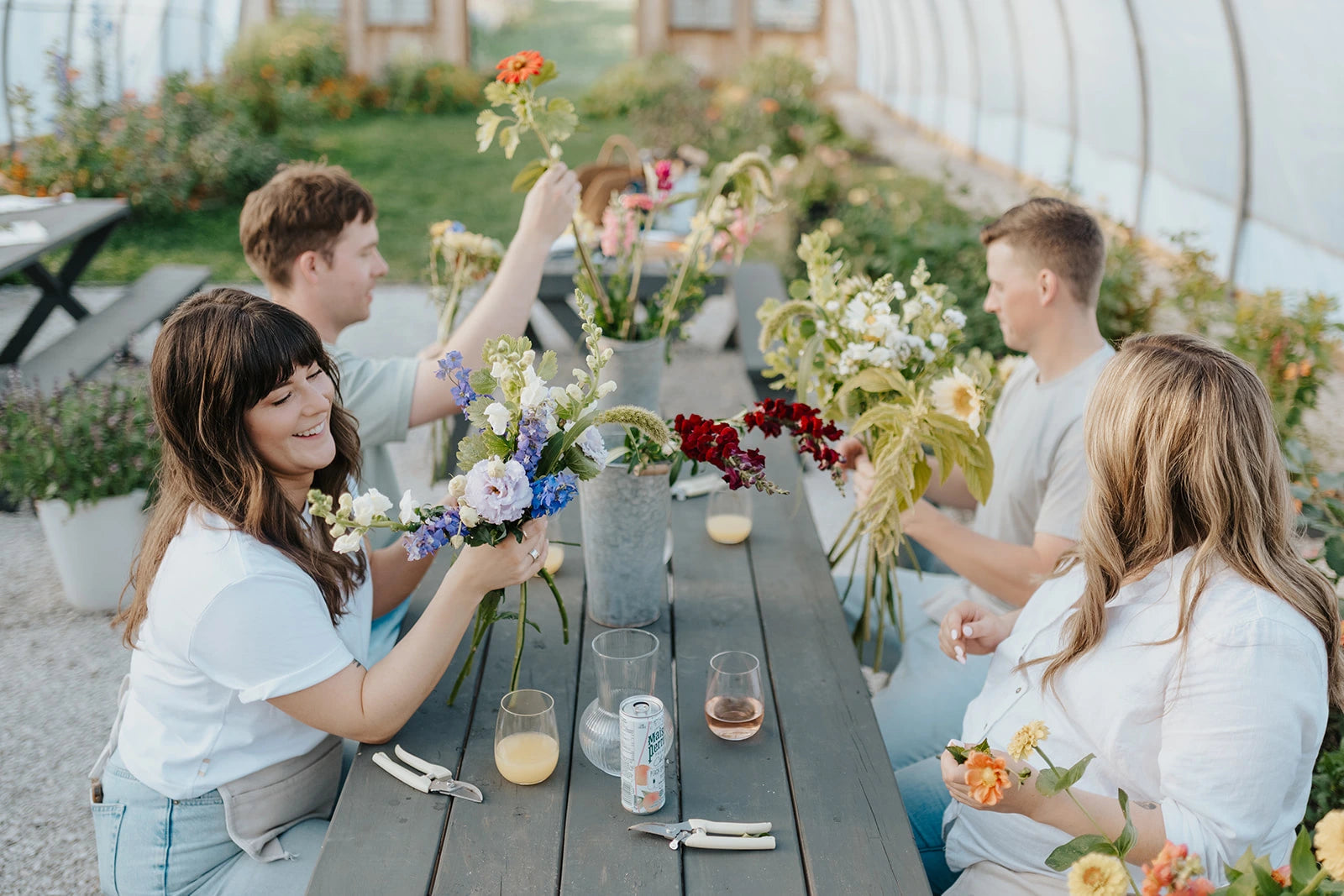 People arranging flowers at a table in a greenhouse setting