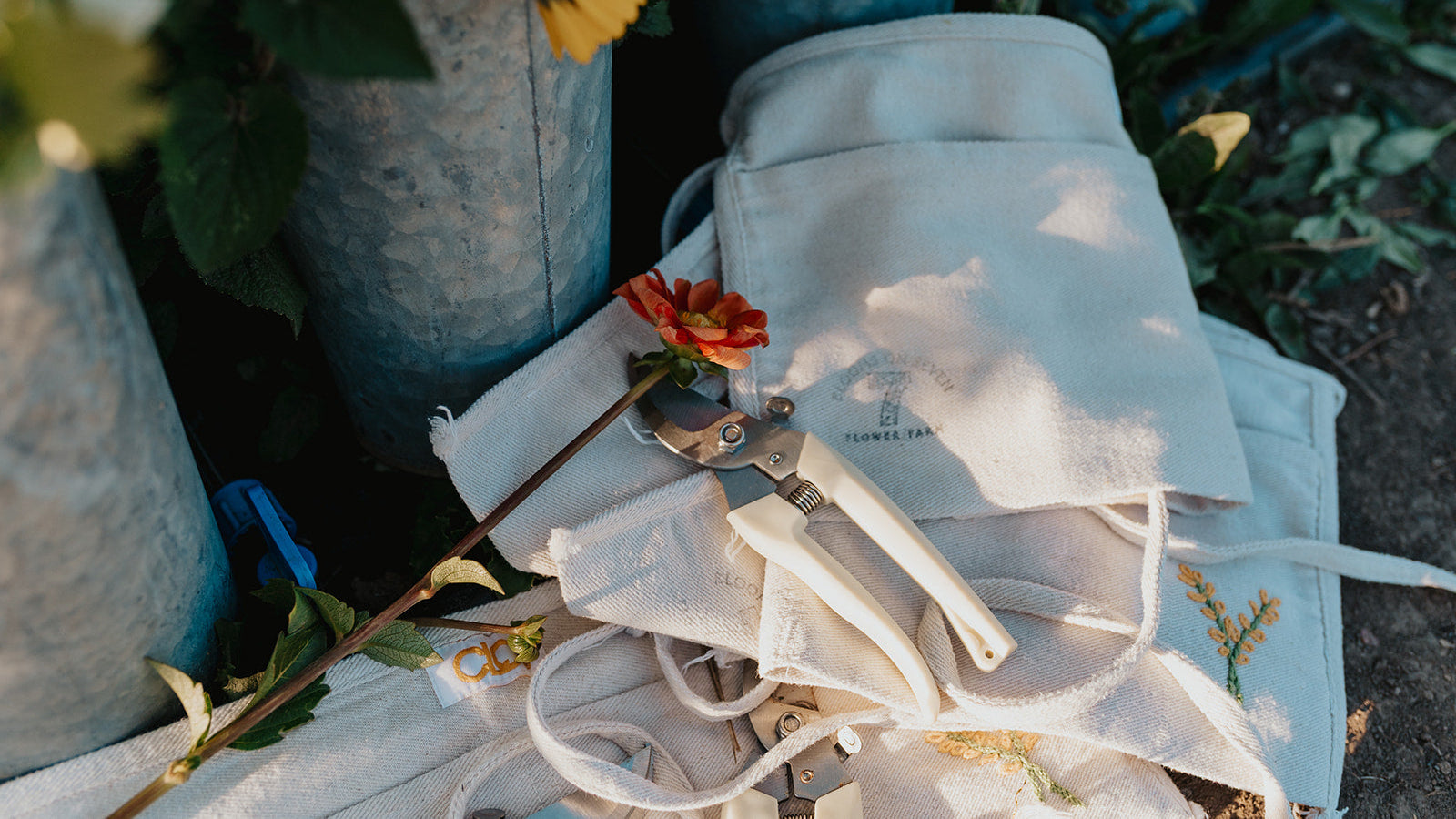 White gardening gloves and tools on a white towel with flowers and plants in the background