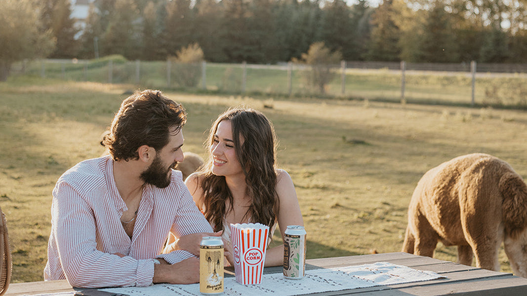 Couple sitting at a picnic table with an alpaca in a field
