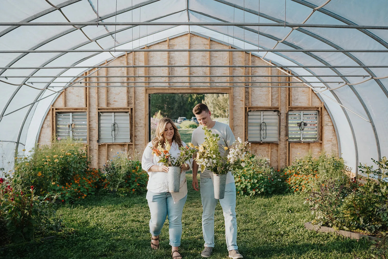 Two people standing in a greenhouse with plants and flowers.