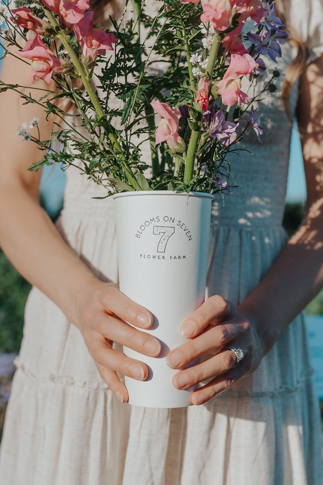 Person holding a white vase with flowers, wearing a light dress.